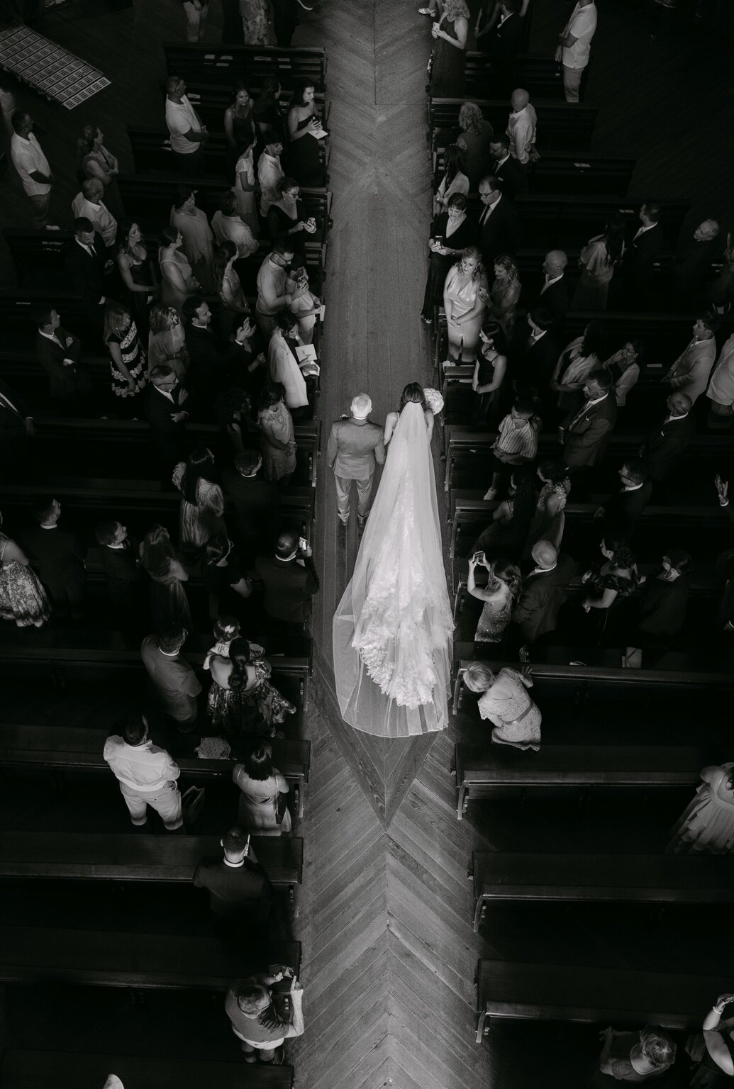 Vista superior da entrada da noiva numa igreja, fotografada a preto e branco.
