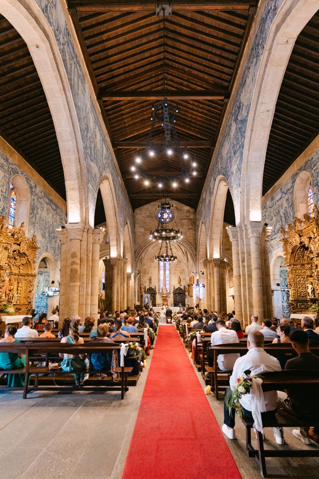 Vista ampla da cerimónia numa igreja histórica, com a nave e o corredor vermelho.