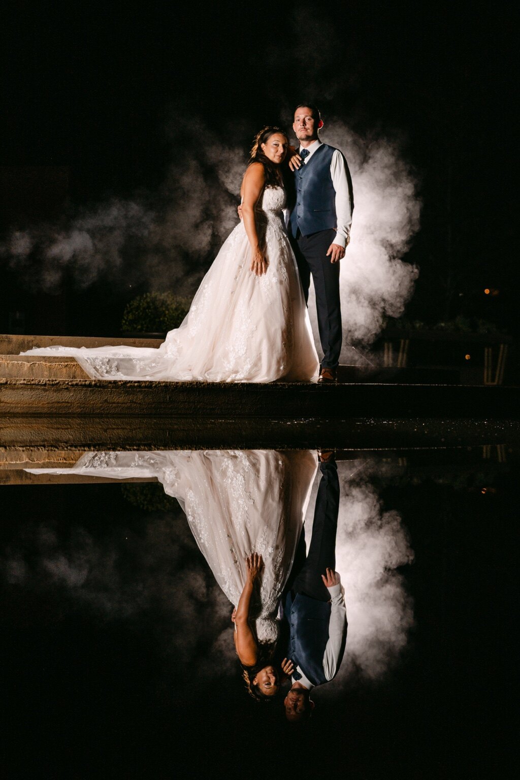 Retrato noturno dos noivos com a sua imagem refletida na água.